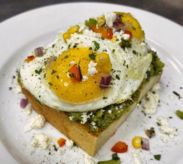 Steak topped with a green spread, two fried eggs, and a mix of chopped vegetables