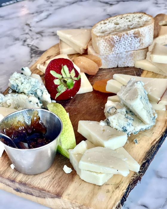 A wooden board with a selection of cheeses, including gorgonzola and hard cheeses, accompanied by a strawberry, fig jam, pear slices, and almonds.