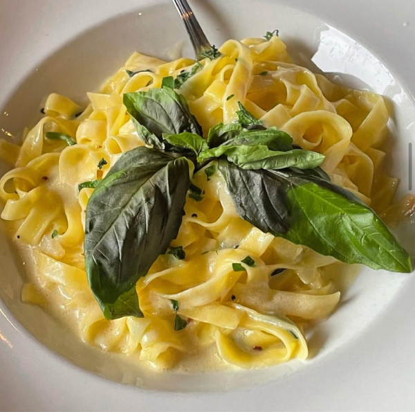 A white bowl of fresh fettuccine pasta with a creamy alfredo sauce, garnished with fresh basil leaves.