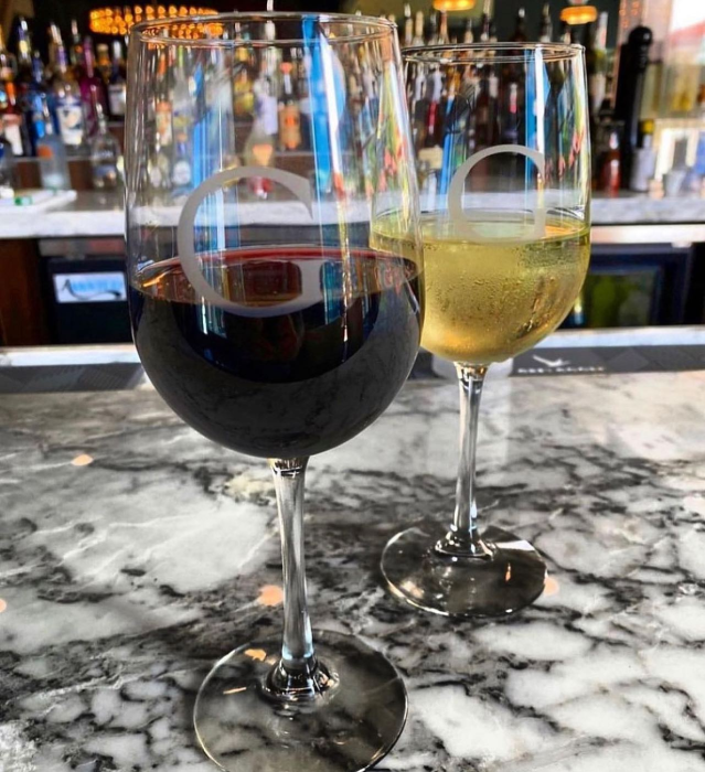 Two stemmed wine glasses on a marble countertop with a blurred bar background.