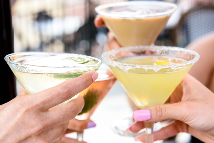Hands toasting three colorful martini and cocktail glasses.