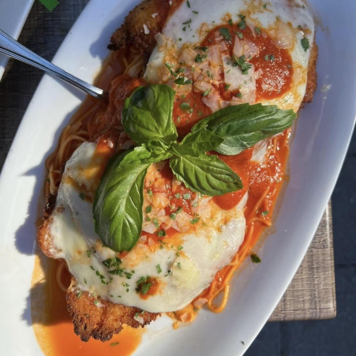 A main course of a breaded cutlet topped with melted cheese, tomato sauce, and fresh basil
