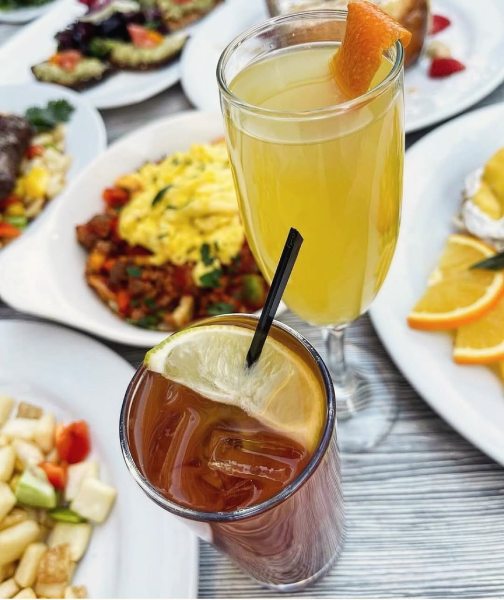 Two handcrafted cocktails next to various plates of food.